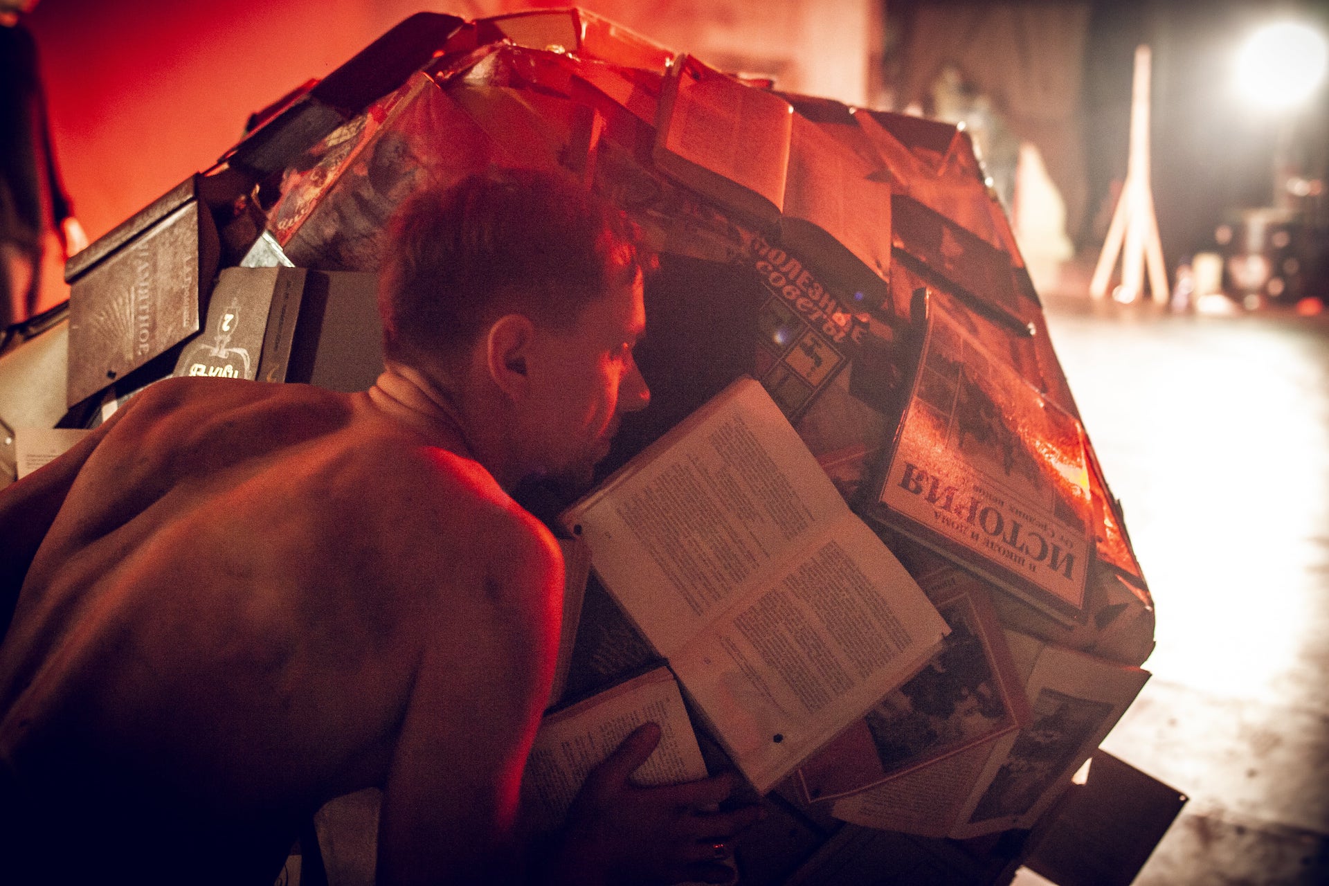 A shirtless performer is lying on a pile of books