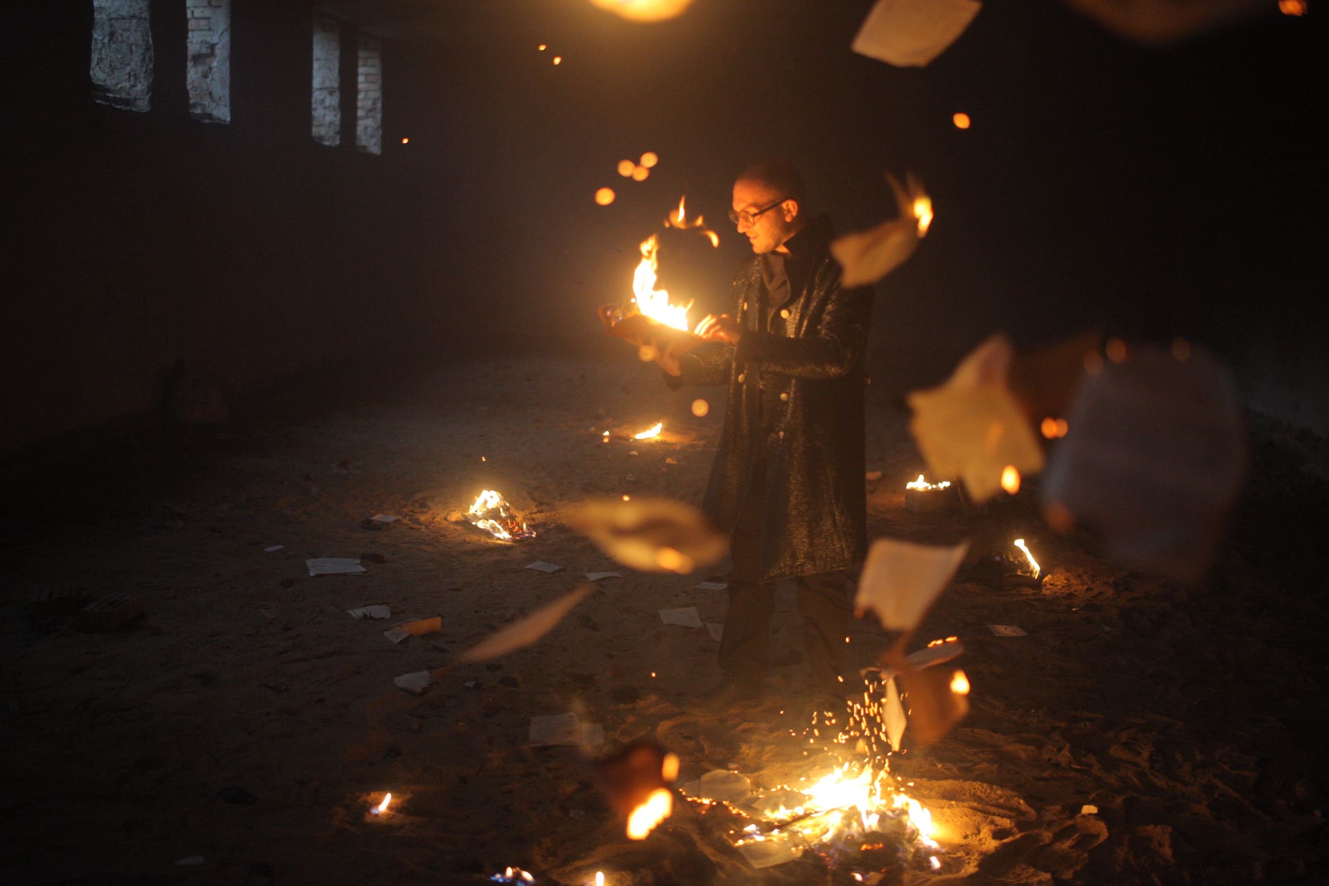 A performer is burning books in a dark room full of sand