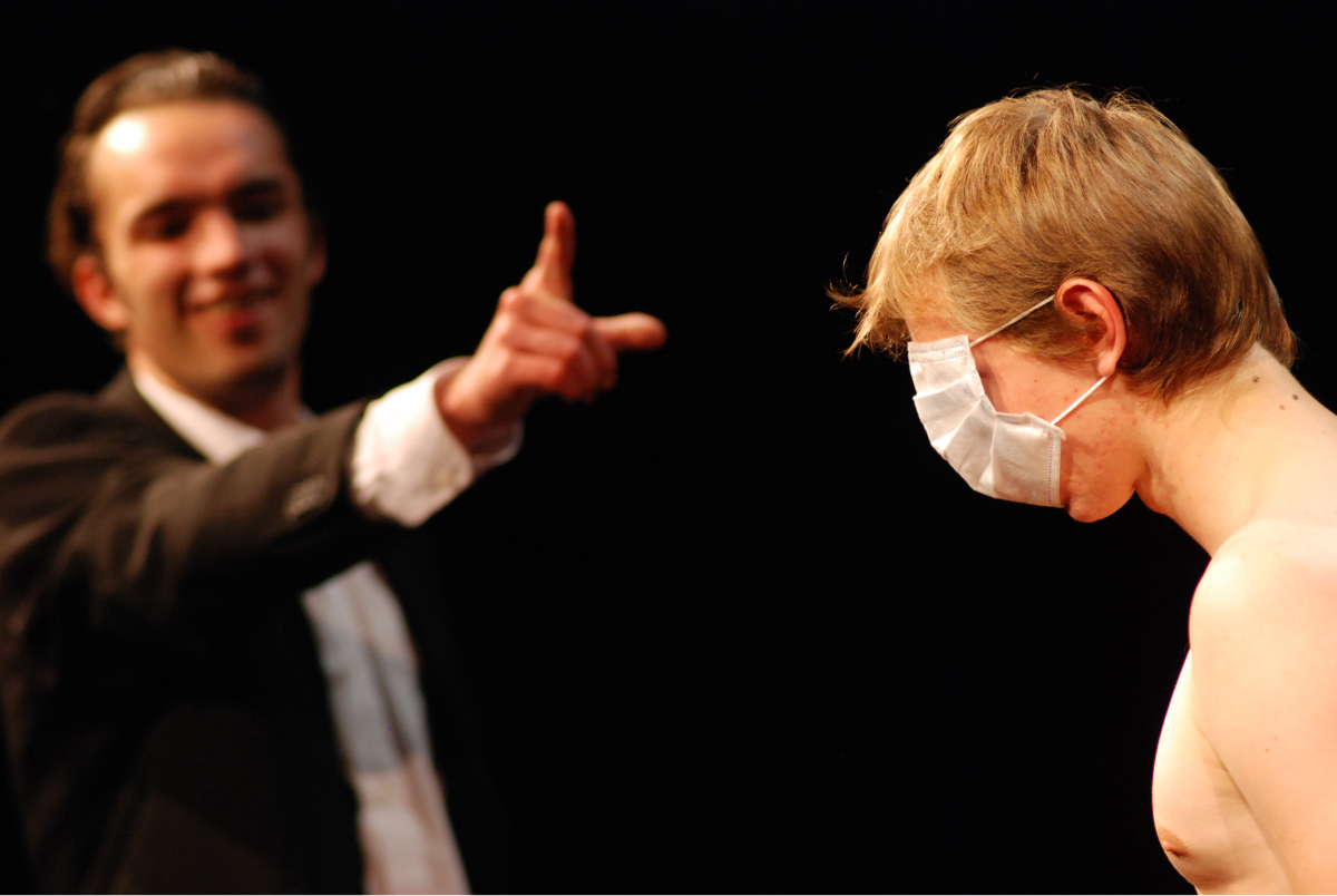 A performer pointing at another performer with a masked covering his eyes and his mouth