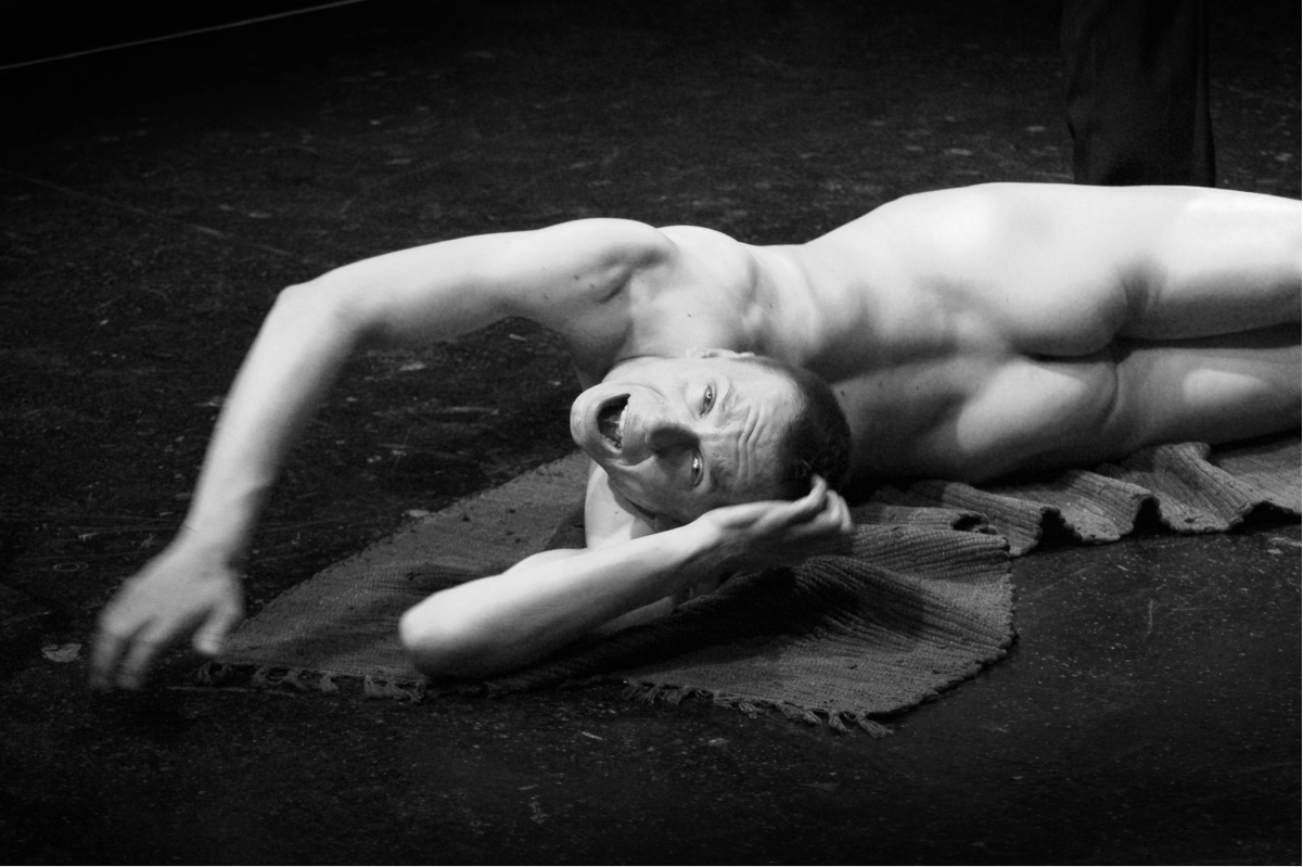A naked man lying down arched back, looking into the camera