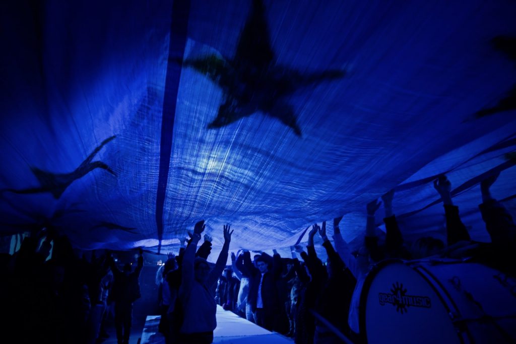 a group of people under a large fabric with star pattern, each lifting the fabric up