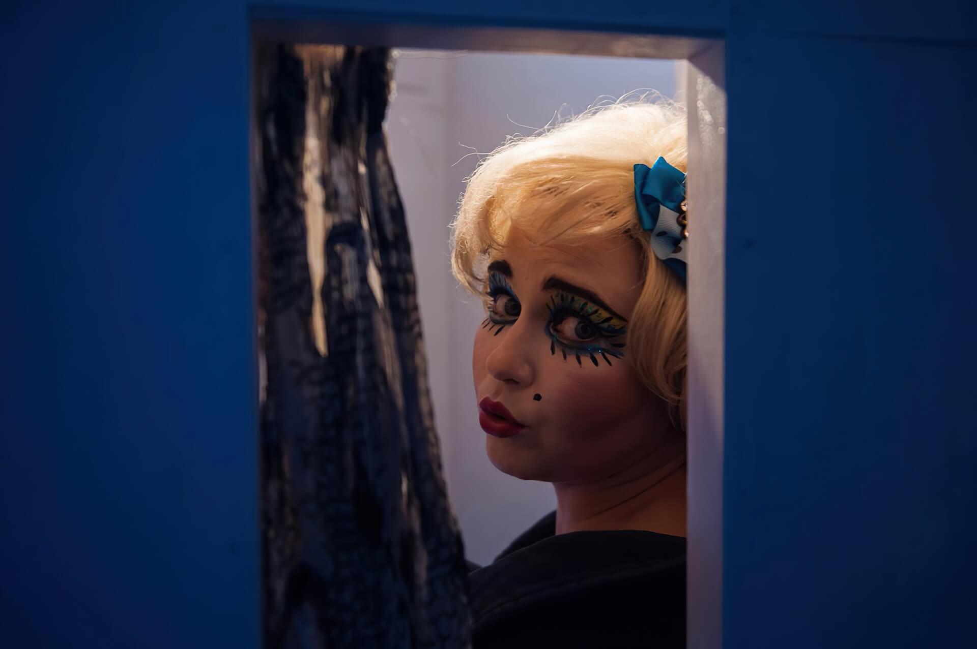 A woman with a heavy makeup looking at the camera through a small window