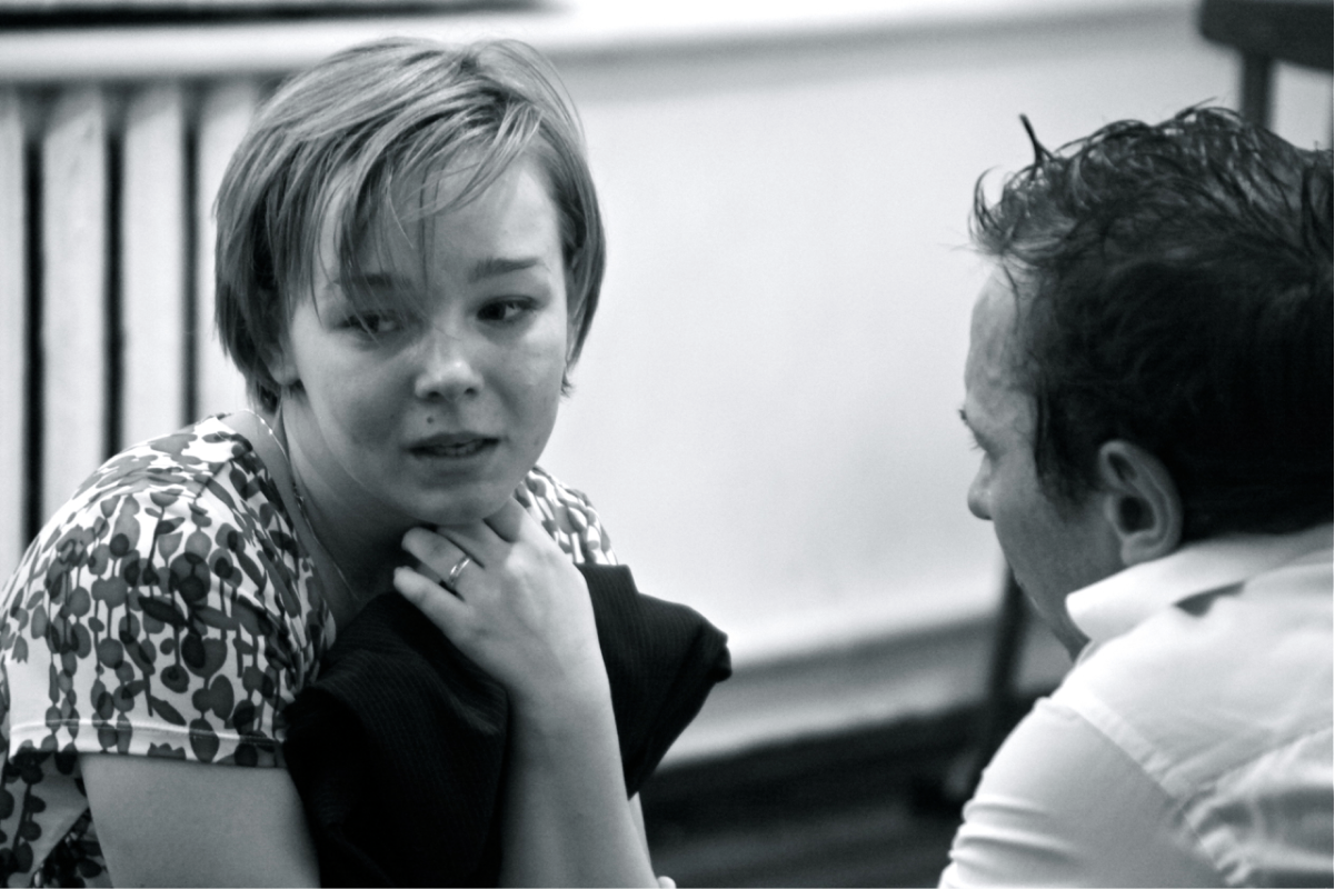 A black and white rehearsal image of two performers talking to each other