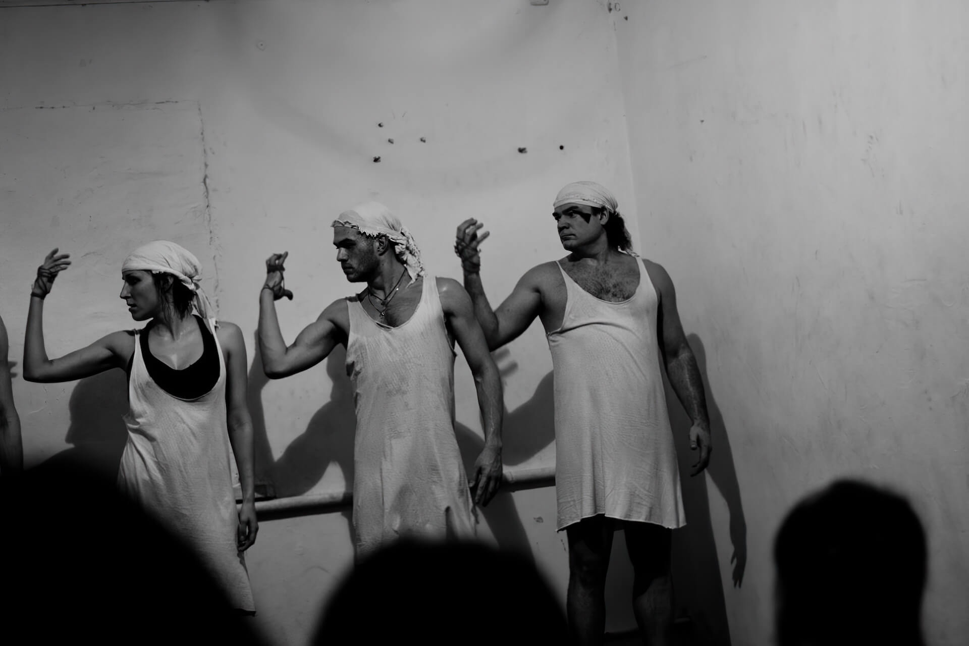 Black and white image of three performers in white garments looking at their grasping right hands.