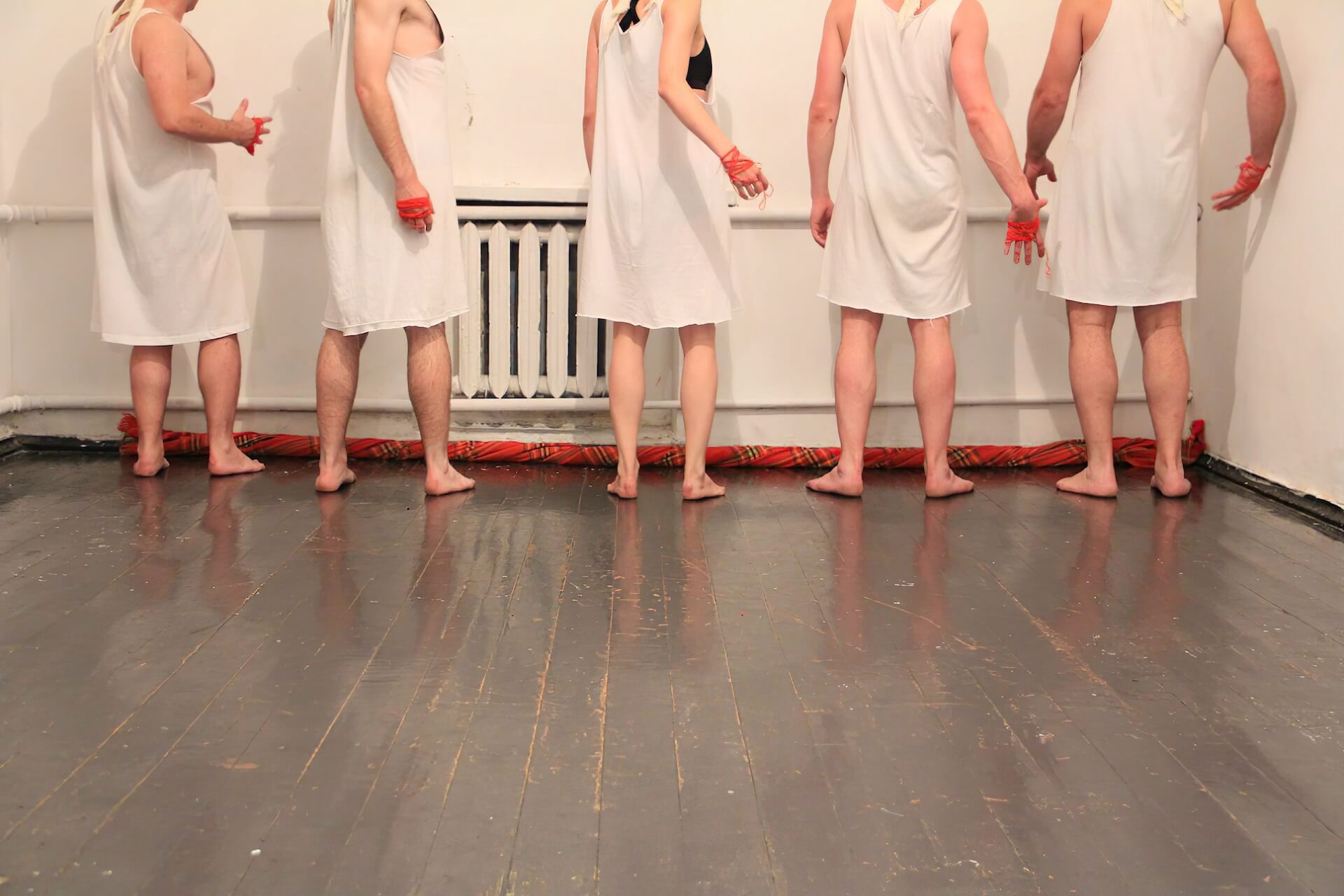 Four performers in white garments are standing by the wall and turning back