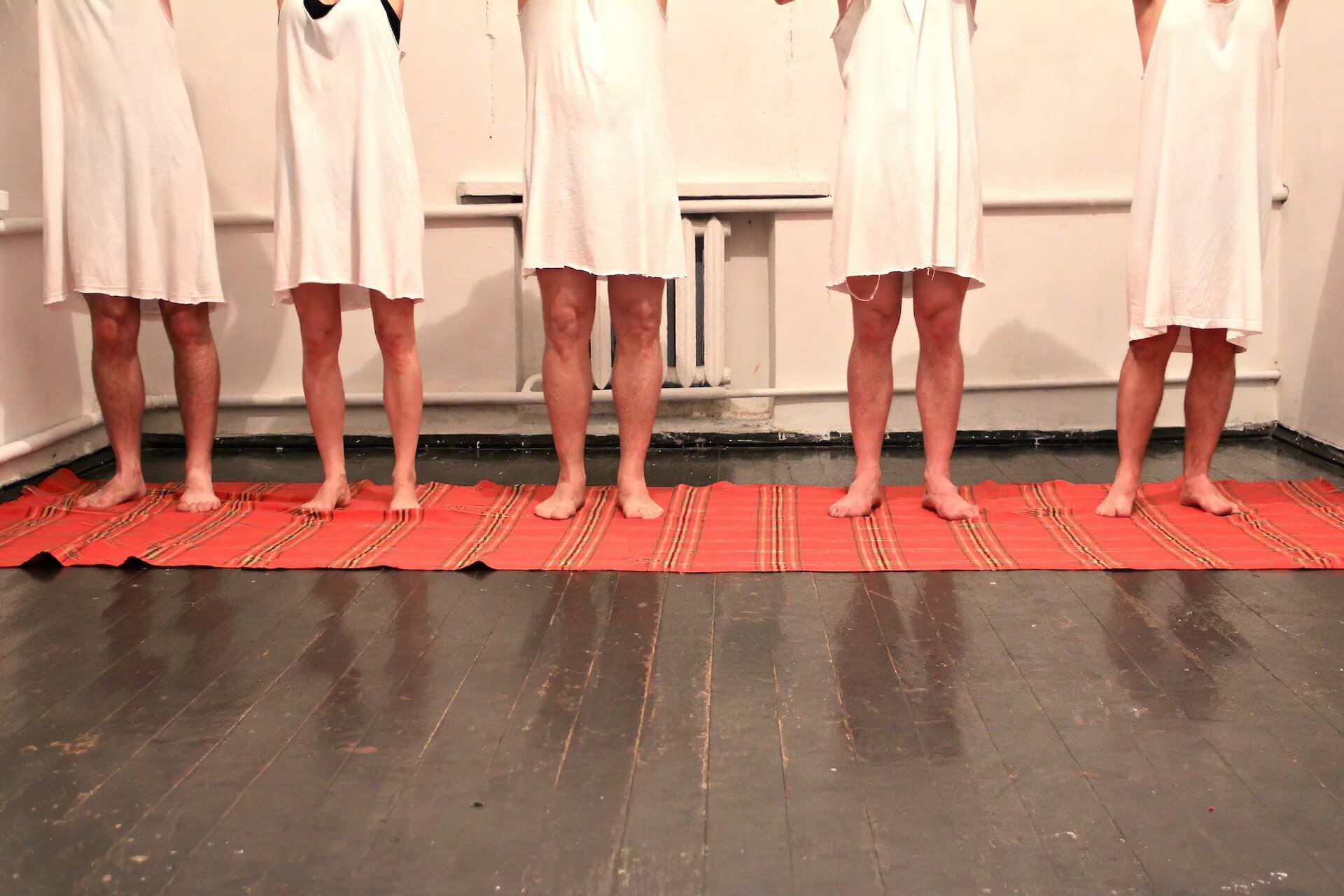 Close up to the feet of the five performers standing in line on a red blanket