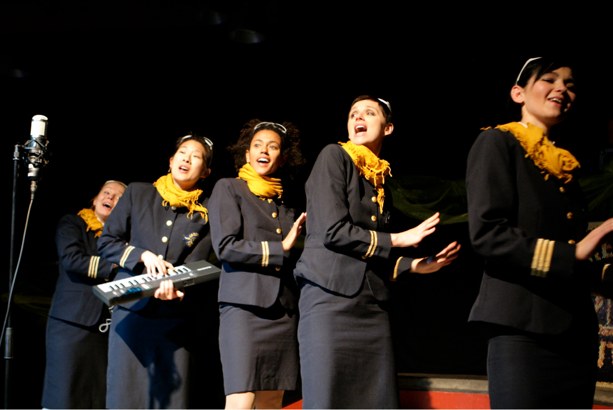 Five performers in uniform are singing, dancing and playing a portable keyboard piano.