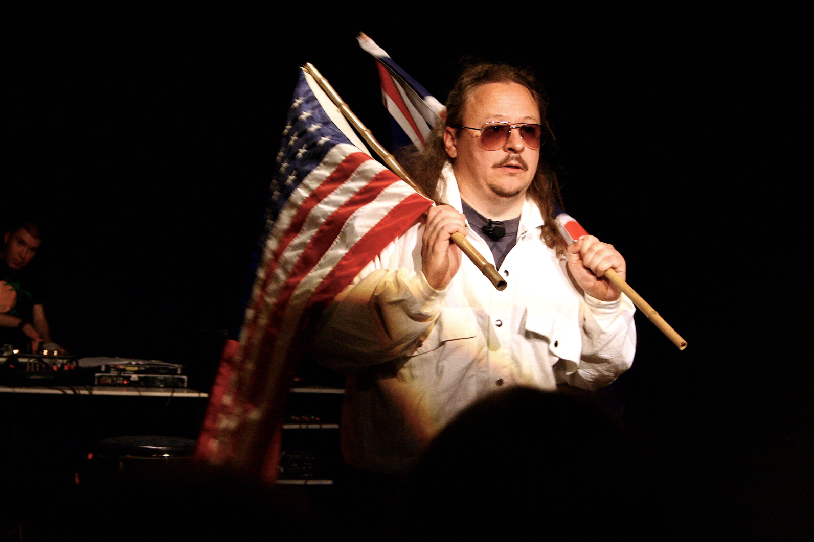 Close up to the performer on stage with sunglasses on holding the flags of USA and Britain on his shoulders