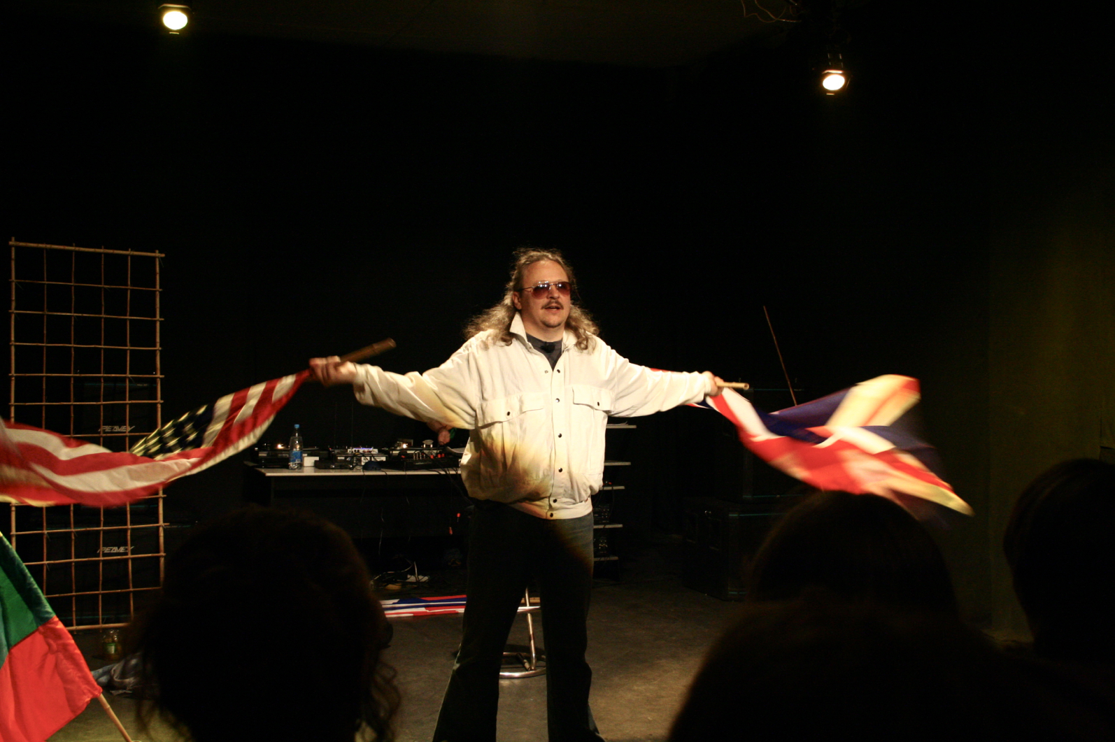 Performer on stage with sunglasses on and swaying flags of Britain and USA.
