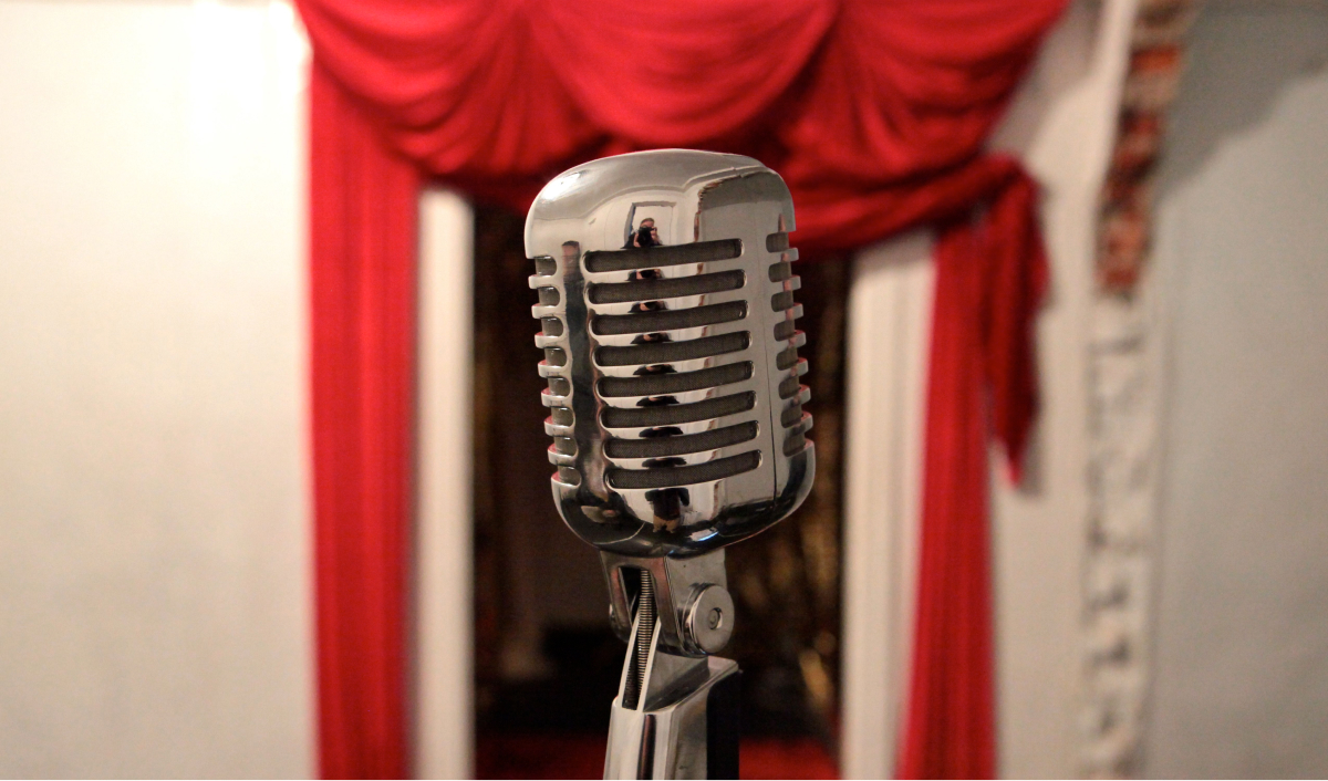 Close up to an old style microphone standing in front of a red stage curtain