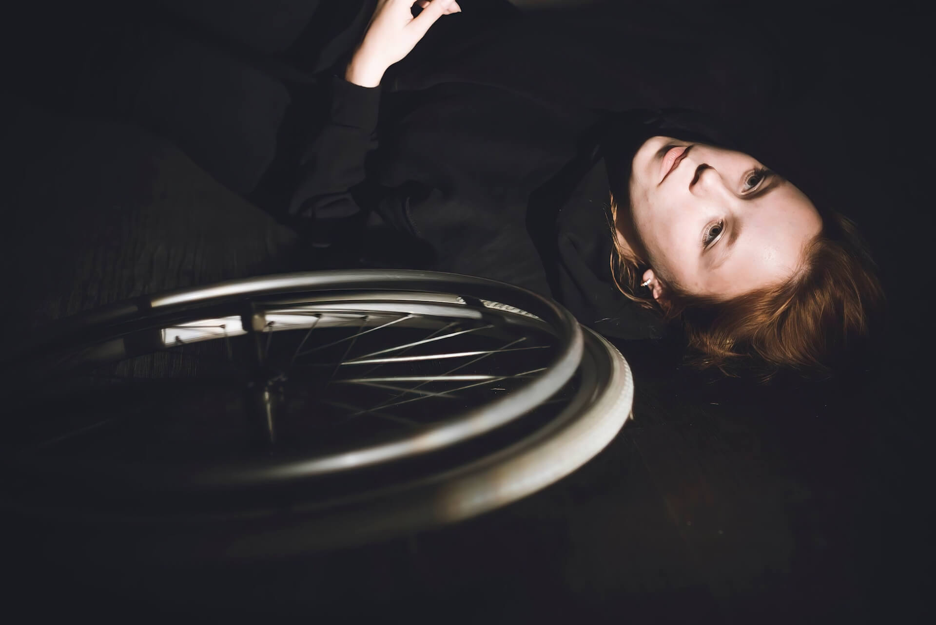 Close up to a performer lying down next to the wheel of a wheelchair.