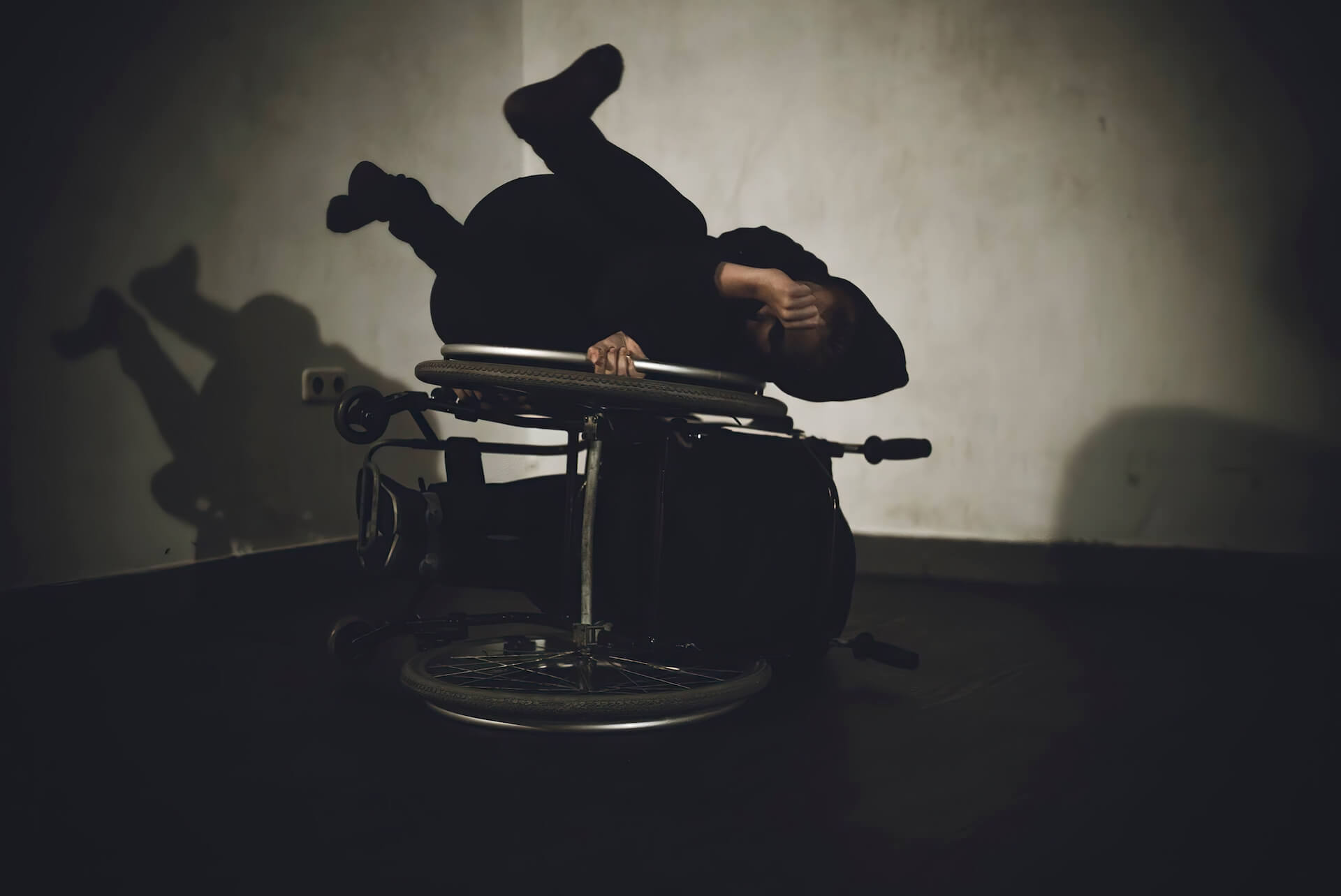 A performer is doing movements with wheelchair. They are lying on top of one wheel of the wheelchair.