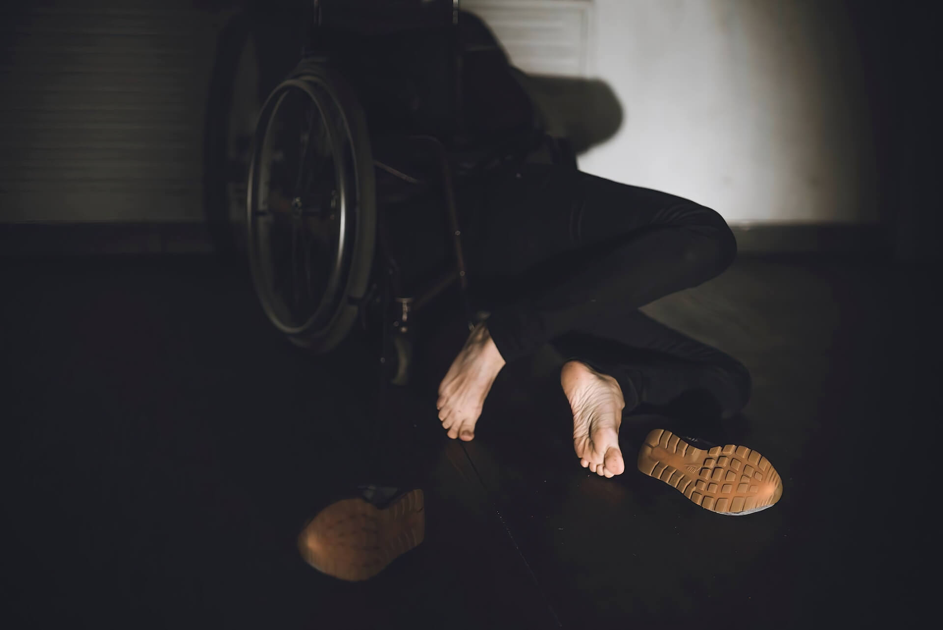 Close up to a performer on a wheelchair who has fallen on the ground with the shoes taken off.