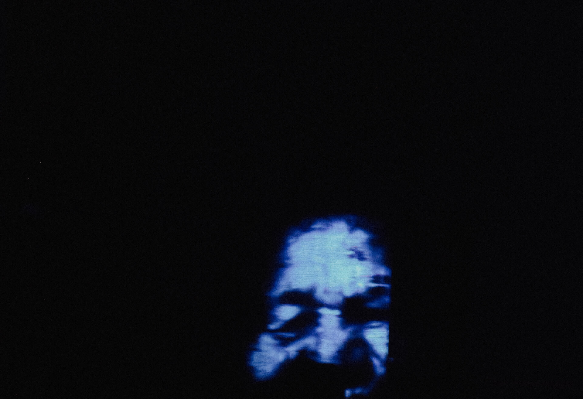 In a dark room a blue face of some one is projected on the wall.