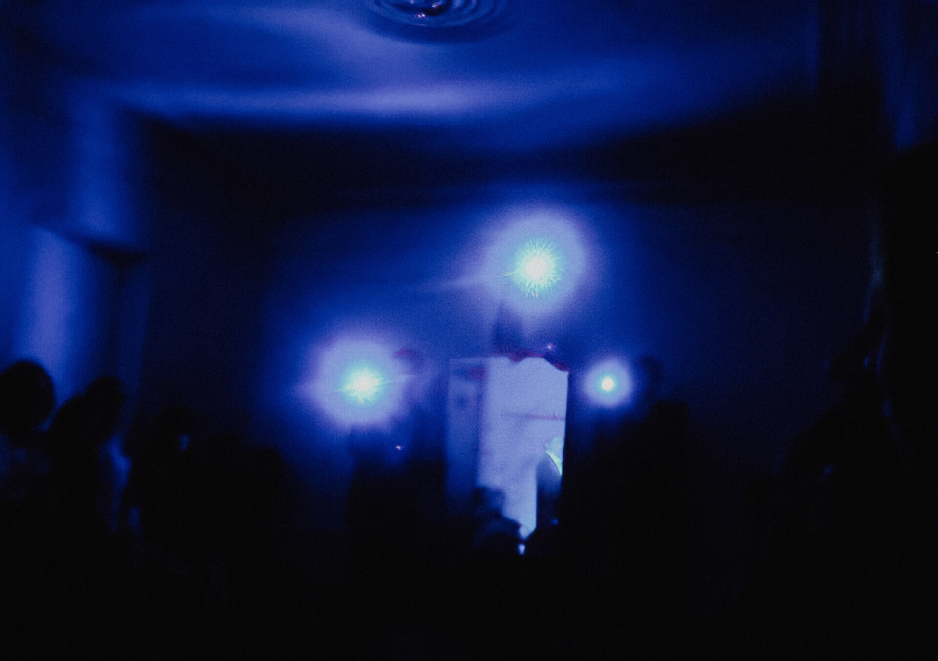 Blurry image of a dark room and three performers each holding light
