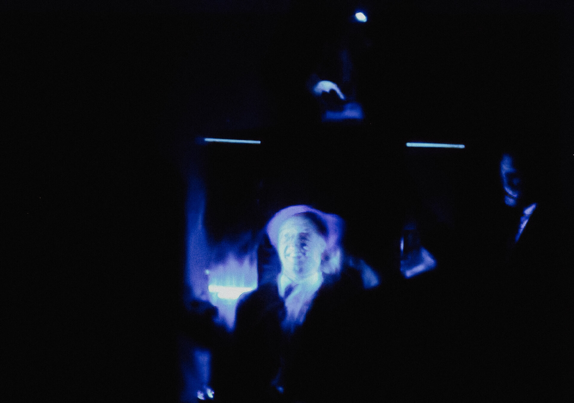 Blurry image of a person smiling. Dimmed blue light is laid on this person