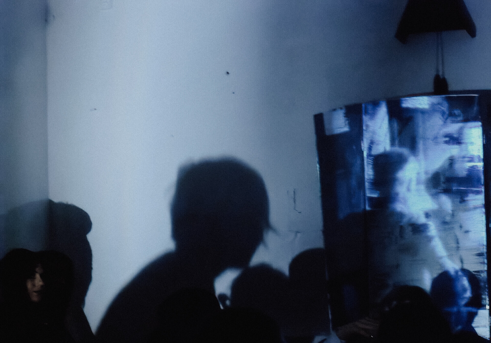 In a dark room slightly hinted with blue lighting. On the right hand side, there is a metal board shaped as like a closet. On the left, there is a shadow of a person