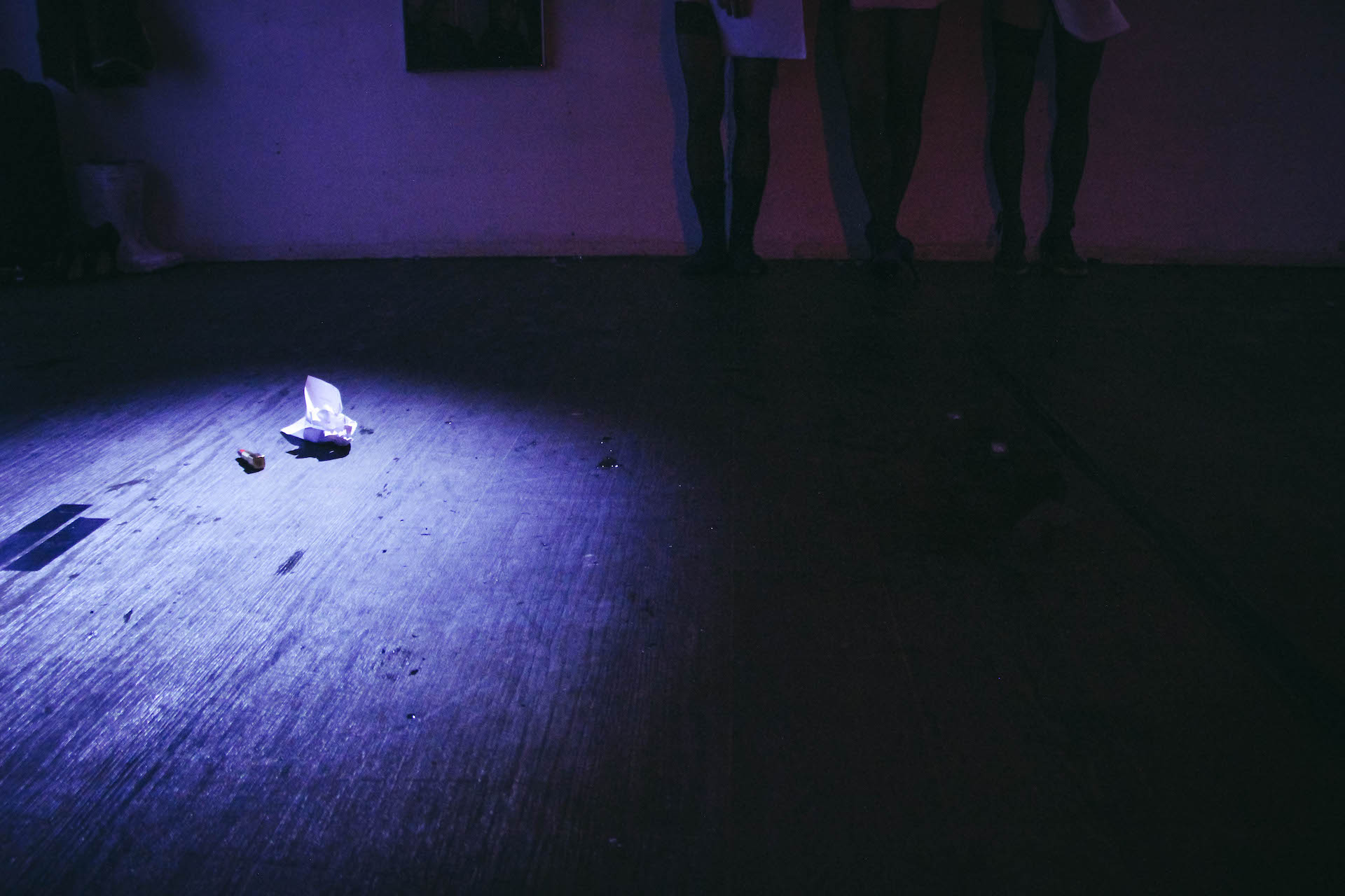 Zoom in to the floor in a dark blue lighted room. On the floor there lies a lipstick and a crumpled piece of paper.