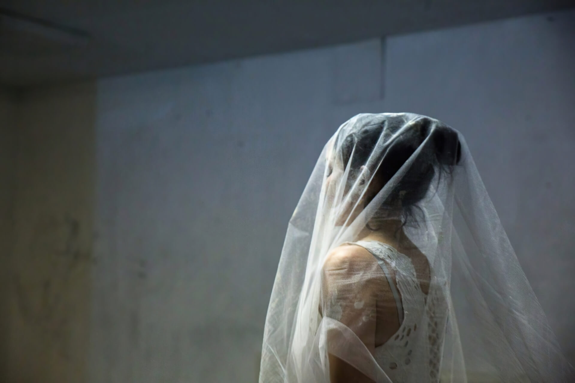 A medium shot of a performer wearing a white dress and a sheer white veil over the head.