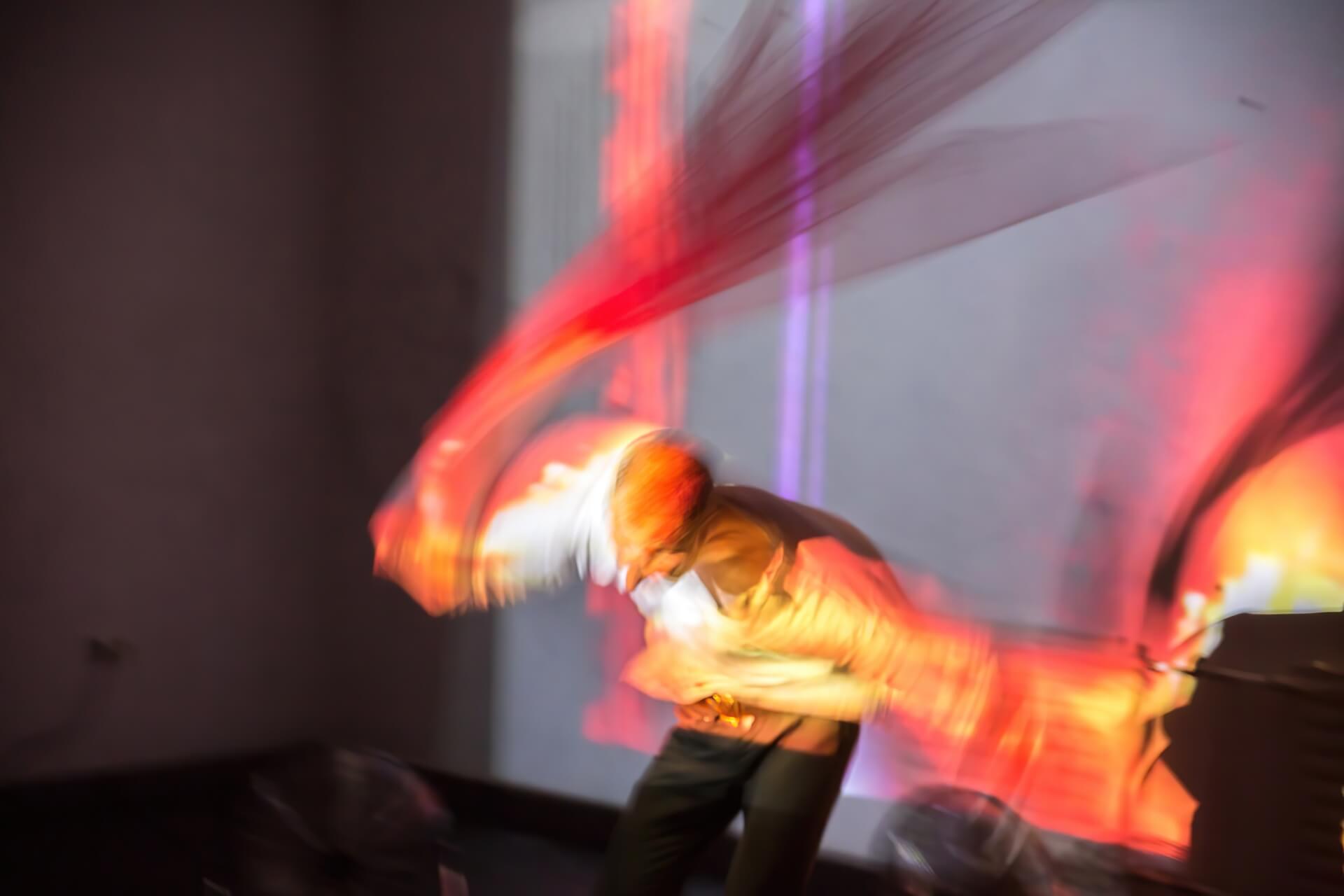 Long exposure shot of a performer dancing aggressively with a sheer red veil.