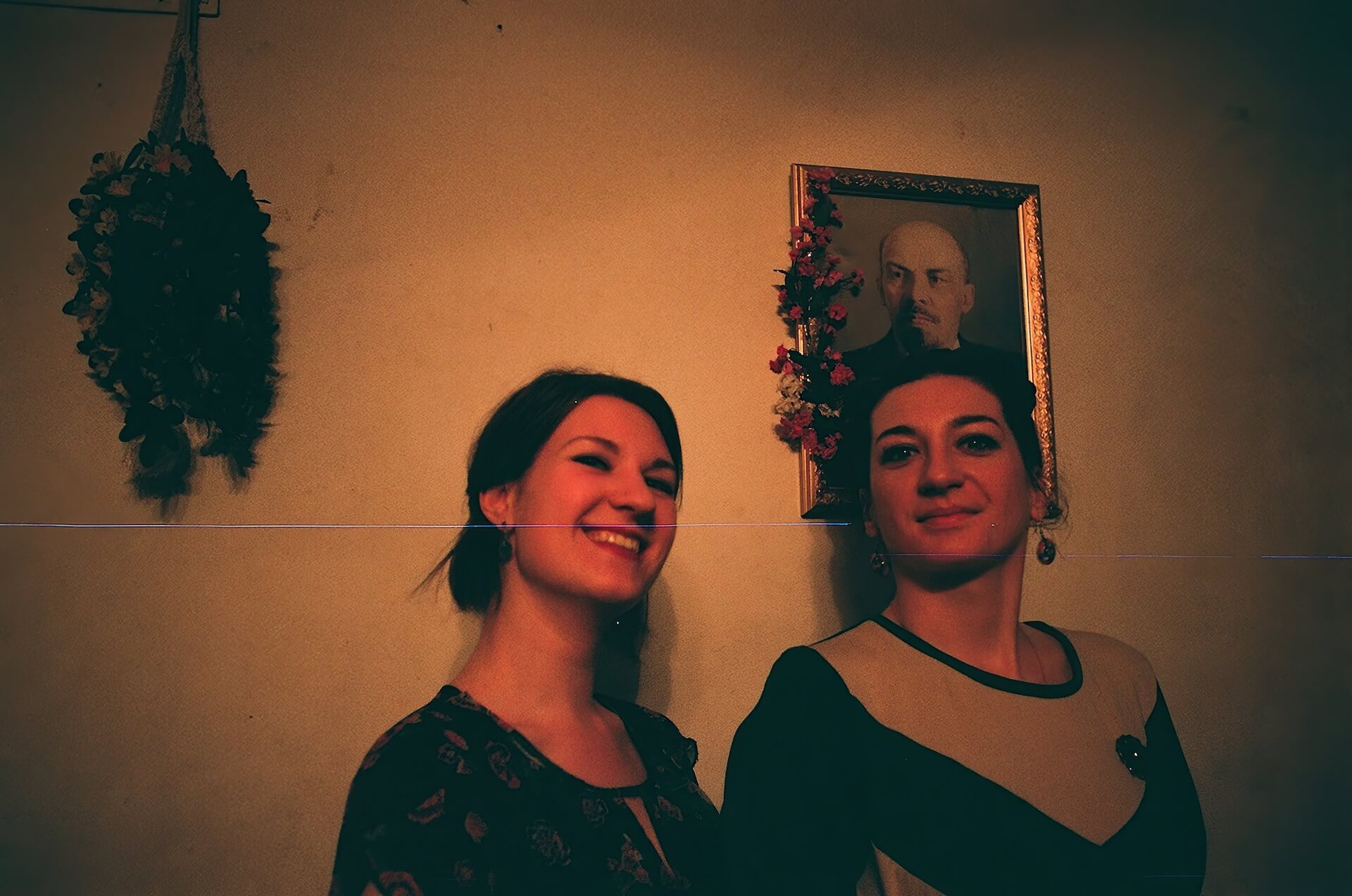 Two people posing for photo in front of a portrait decorated with flowers